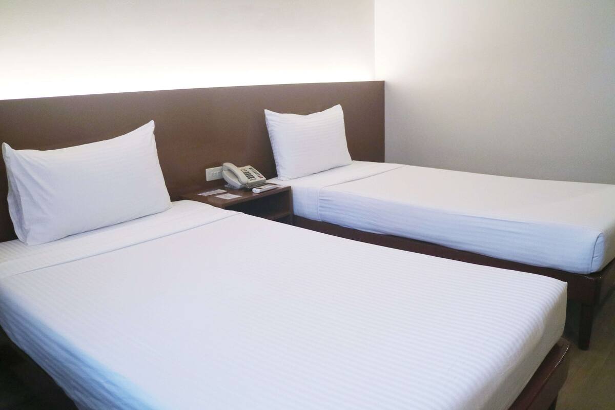 Two single beds with white linens, a bedside telephone, and a brown headboard.