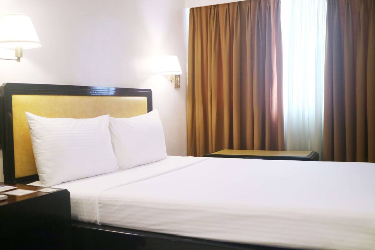 A hotel room with a large bed, two bedside lamps, a nightstand, and a window with curtains.