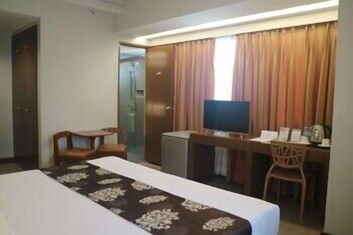 A hotel room with a bed, a desk with a computer, a television, and a chair.
