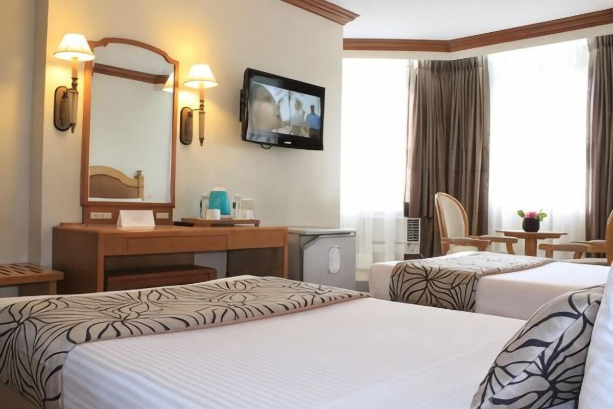 A hotel room with two beds, a desk, a television, and a window with curtains.