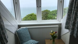 A corner room with a view of the sea, a chair, a small table with a vase of flowers, and a radiator. - Borthalan Hotel (St Ives)