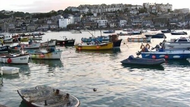 A harbor with various boats docked, a small boat in the foreground, and buildings in the background. - Borthalan Hotel (St Ives)