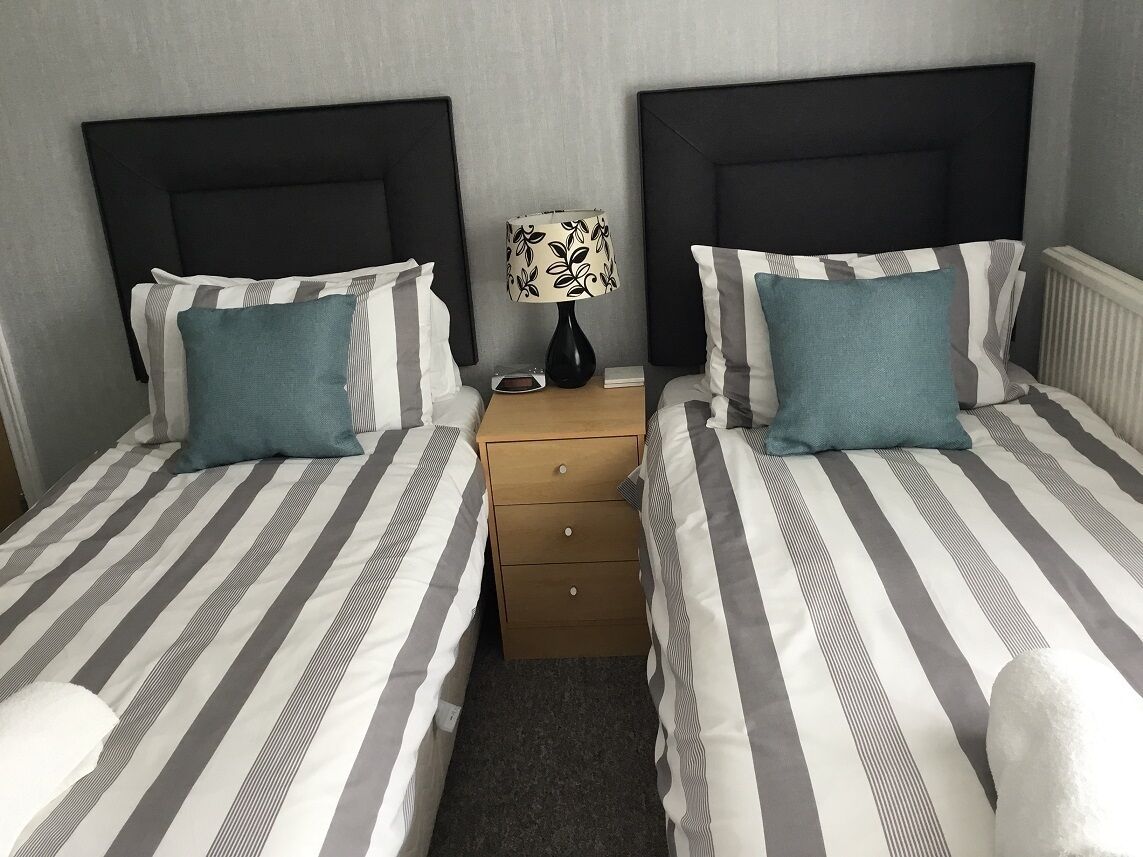 A double bed with striped bedding, a bedside table with a lamp, and a nightstand with drawers.