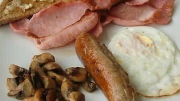 A plate of breakfast food including bacon, sausages, mushrooms, toast, and eggs.