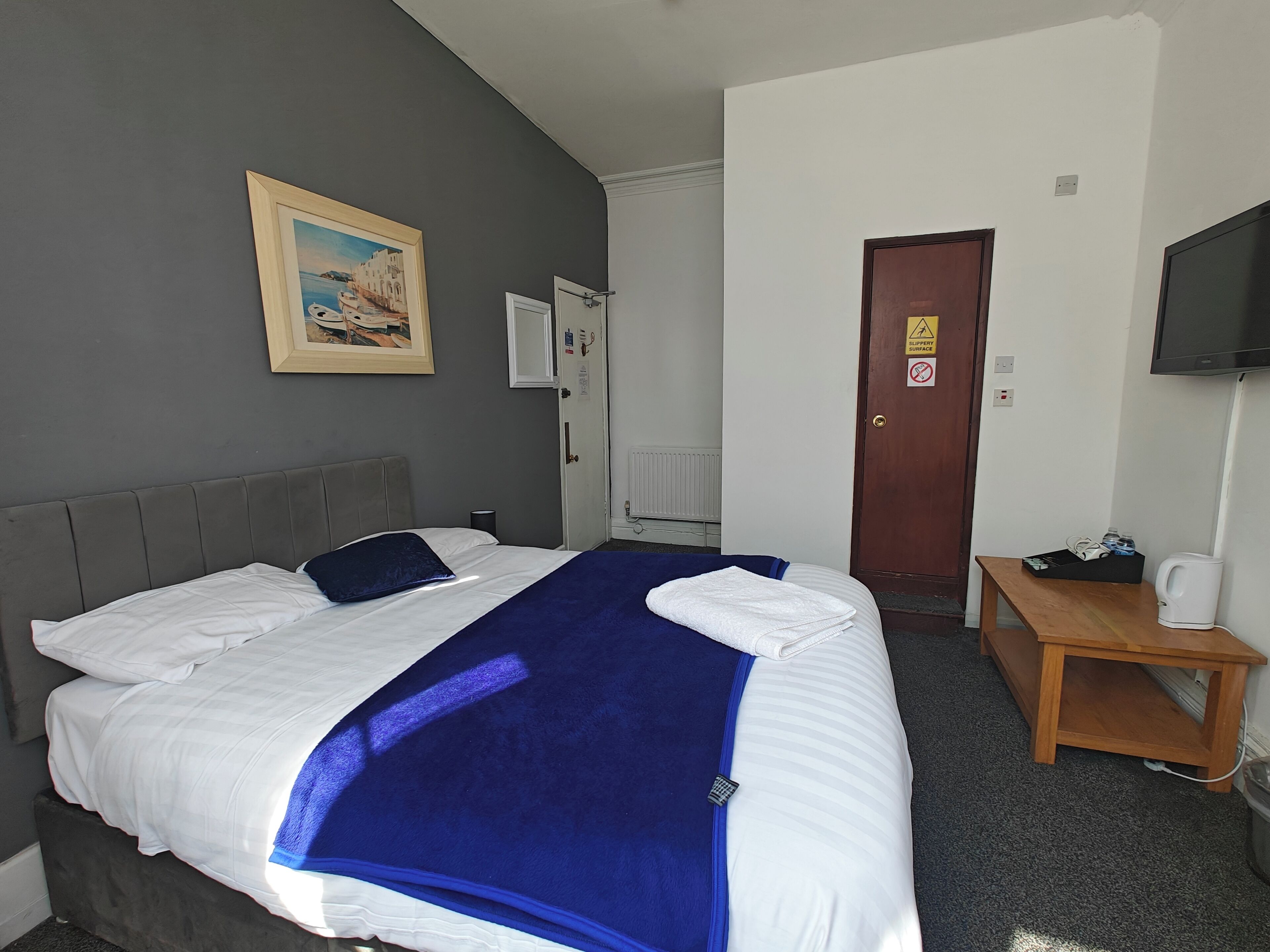 A hotel room with a bed, a wooden nightstand, a television, and a painting on the wall.
