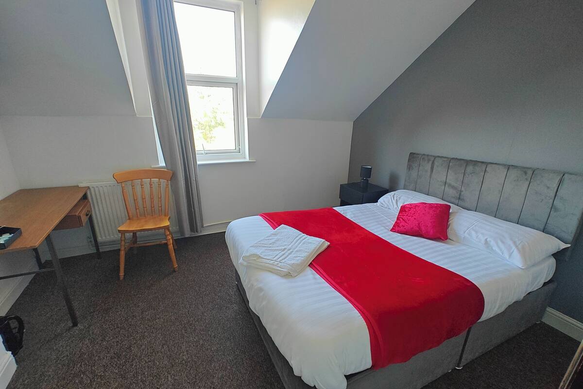 A bedroom with a bed, a desk, a chair, and a window.