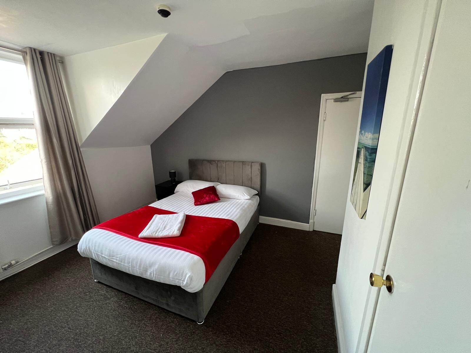 A bedroom with a bed, a nightstand, a window with curtains, and a door.