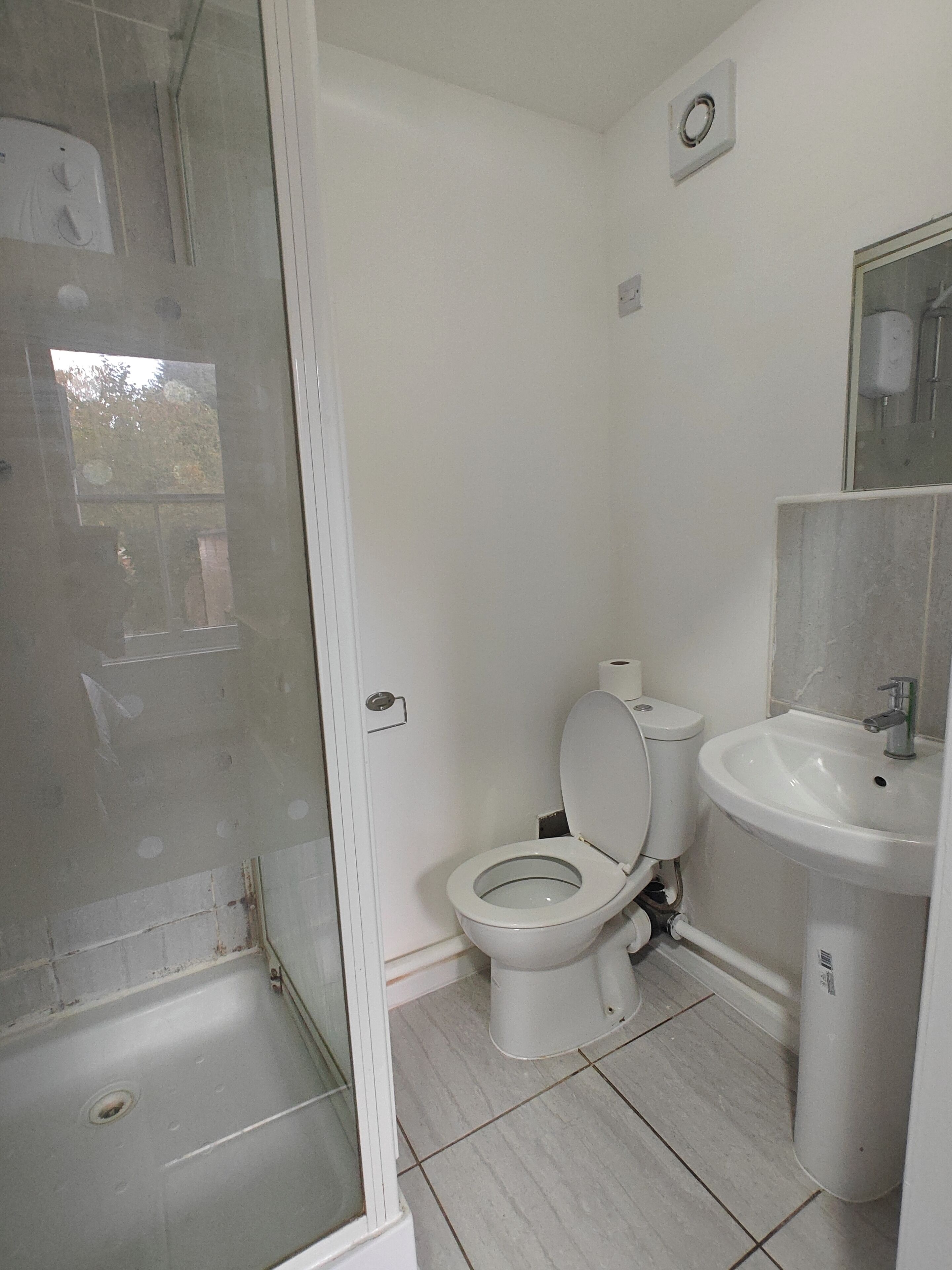 Un baño con inodoro, lavamanos y zona de ducha con mampara de vidrio.