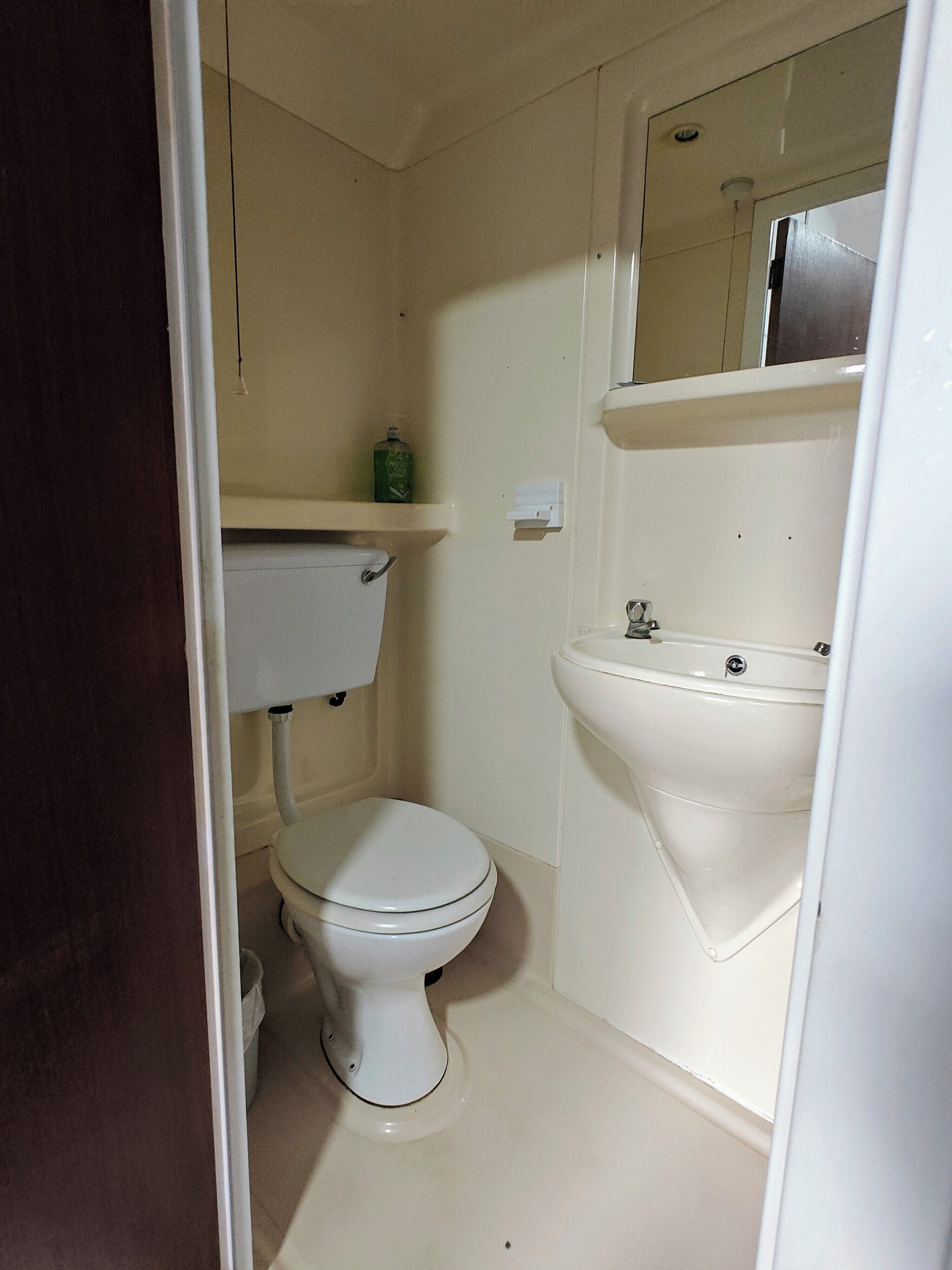 A small, basic bathroom with a toilet, sink, and mirror.