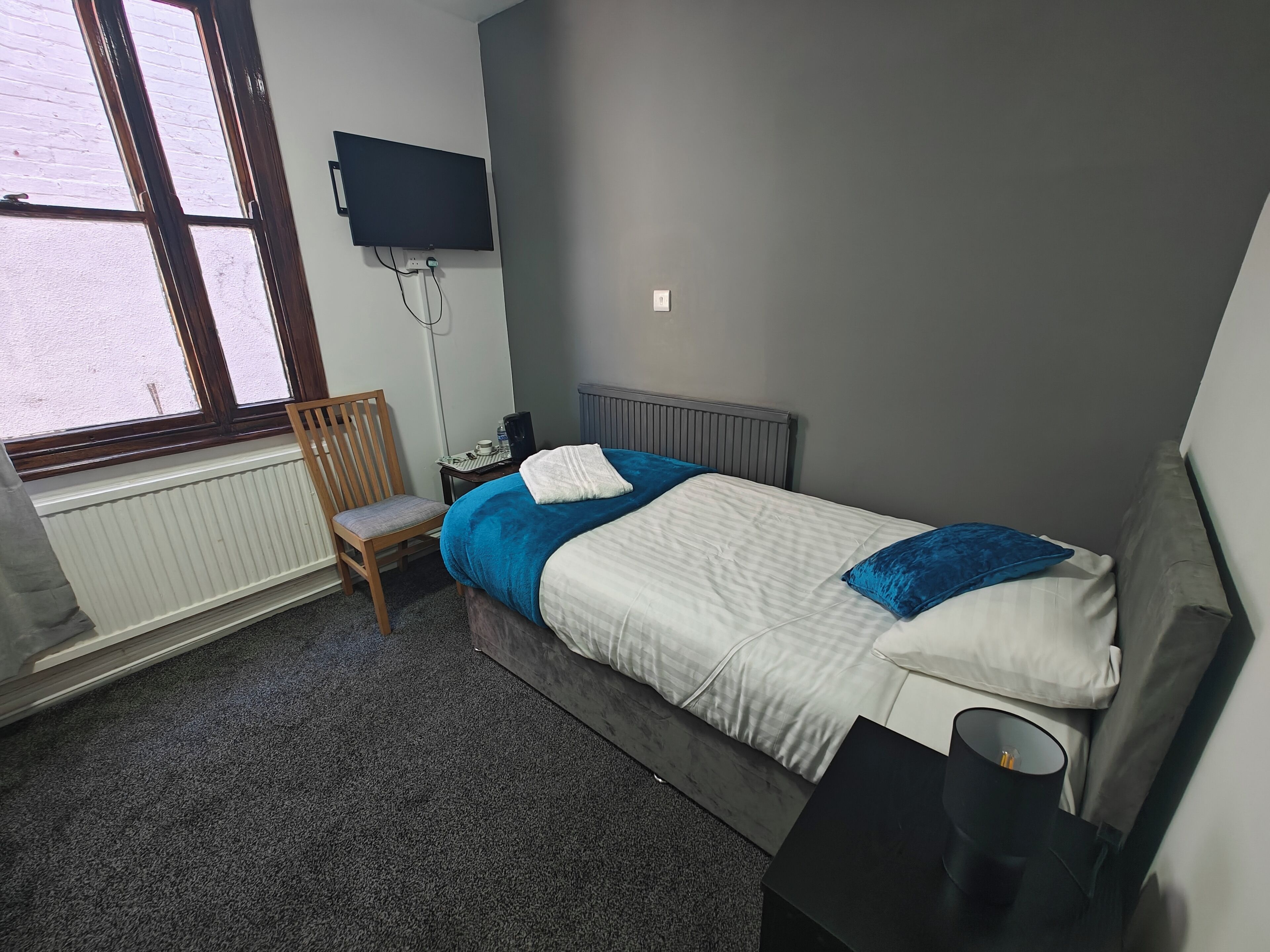A bedroom with a bed, a chair, a desk, a TV, and a radiator.