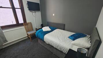 A bedroom with a bed, a chair, a desk, a TV, and a radiator.