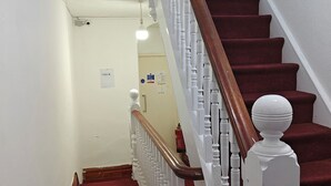 A staircase with a wooden handrail and white balusters, leading to a landing with a white ceiling and a light fixture. - Campbell's Guest House (Leicester)