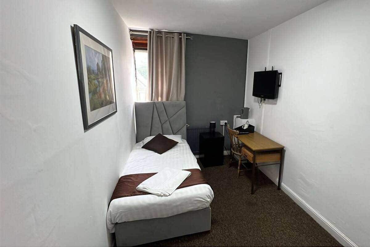 A small, compact room with a bed, a desk, a chair, a television, and a window with curtains.