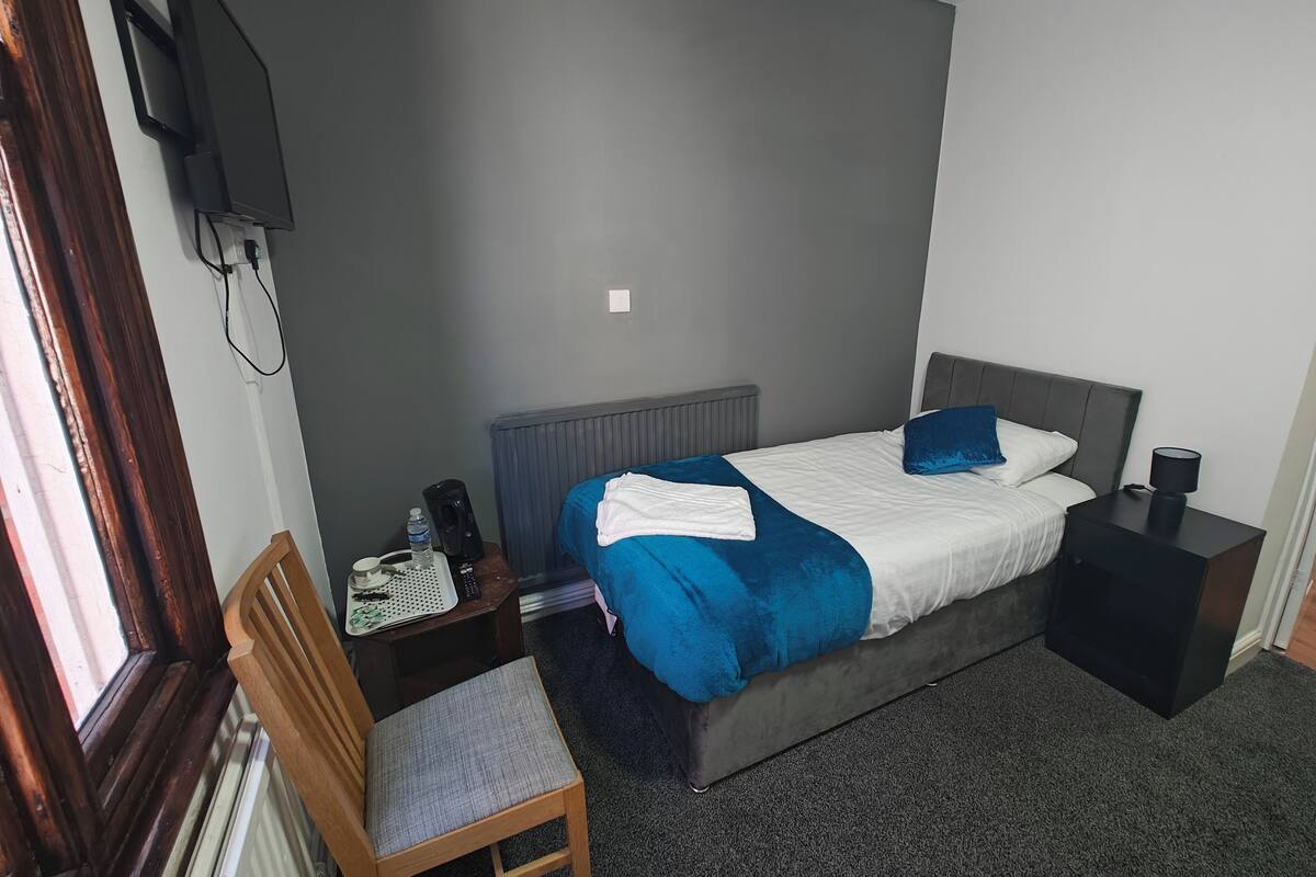 A neatly arranged hotel room with a bed, bedside table, chair, and a television mounted on the wall.