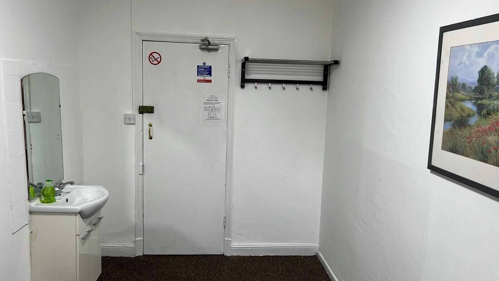 Eine weiße Tür mit einem Feuerausgangsschild, ein kleines Waschbecken mit Spiegel und ein Handtuchhalter.