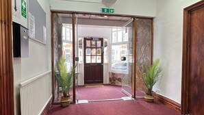 A hotel entrance with a red carpet, a glass door, and two potted plants. - Campbell's Guest House (Leicester)