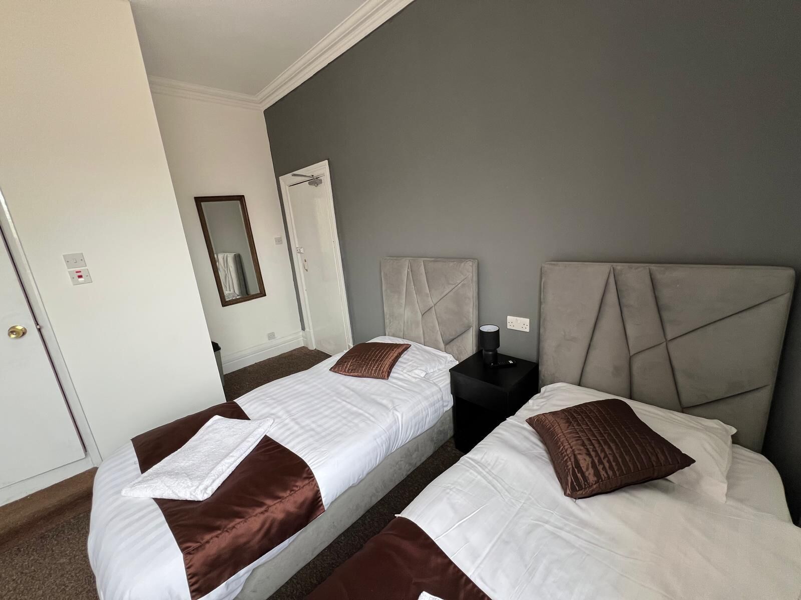Ein Hotelzimmer mit zwei Betten, einem Nachttisch, einem Spiegel und einer Tür.