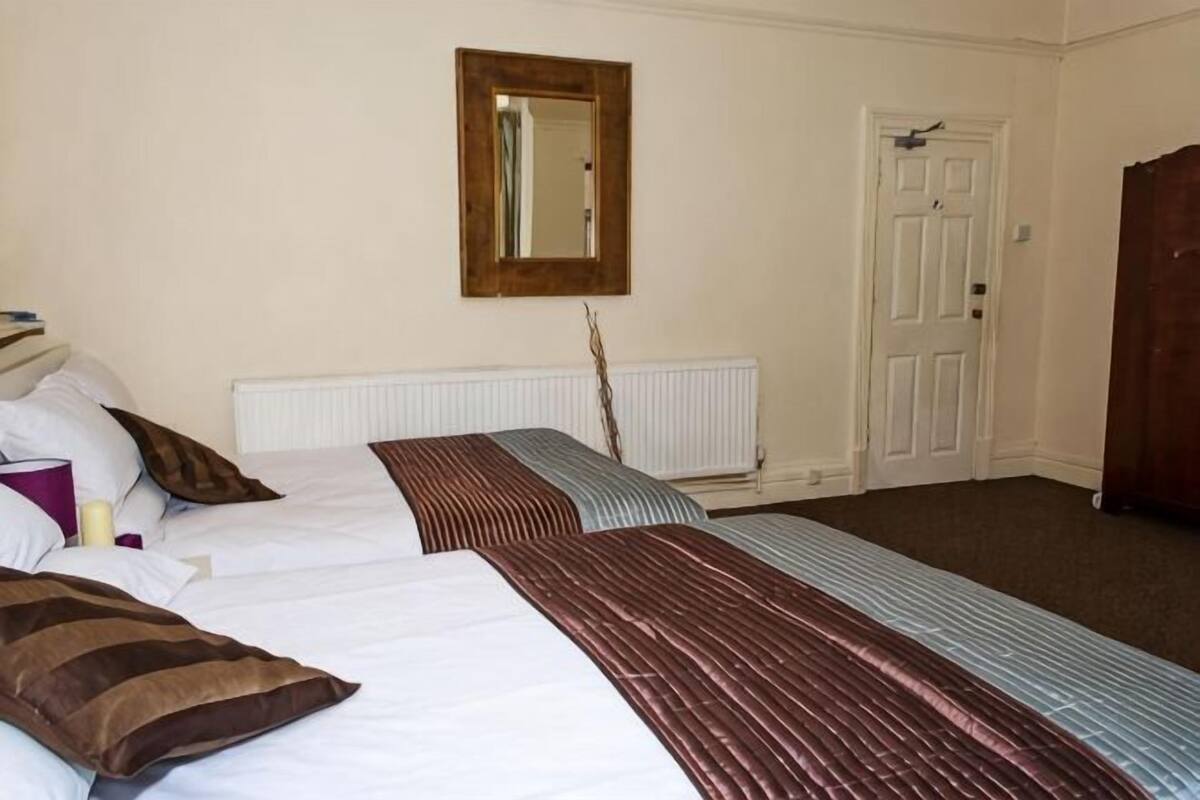 A room with two beds, a mirror, a radiator, and a door.