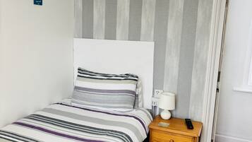 Une chambre à coucher avec un lit, une table de chevet, une lampe et une porte.