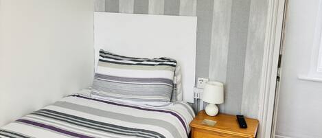 A bedroom with a bed, a nightstand, a lamp, and a door.