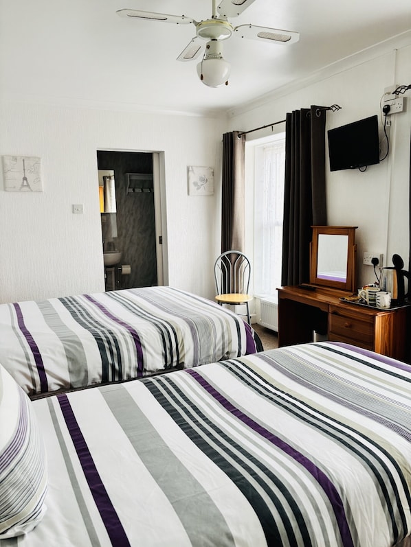 A bedroom with two beds, a desk, a chair, a ceiling fan, a TV, and a window with curtains.