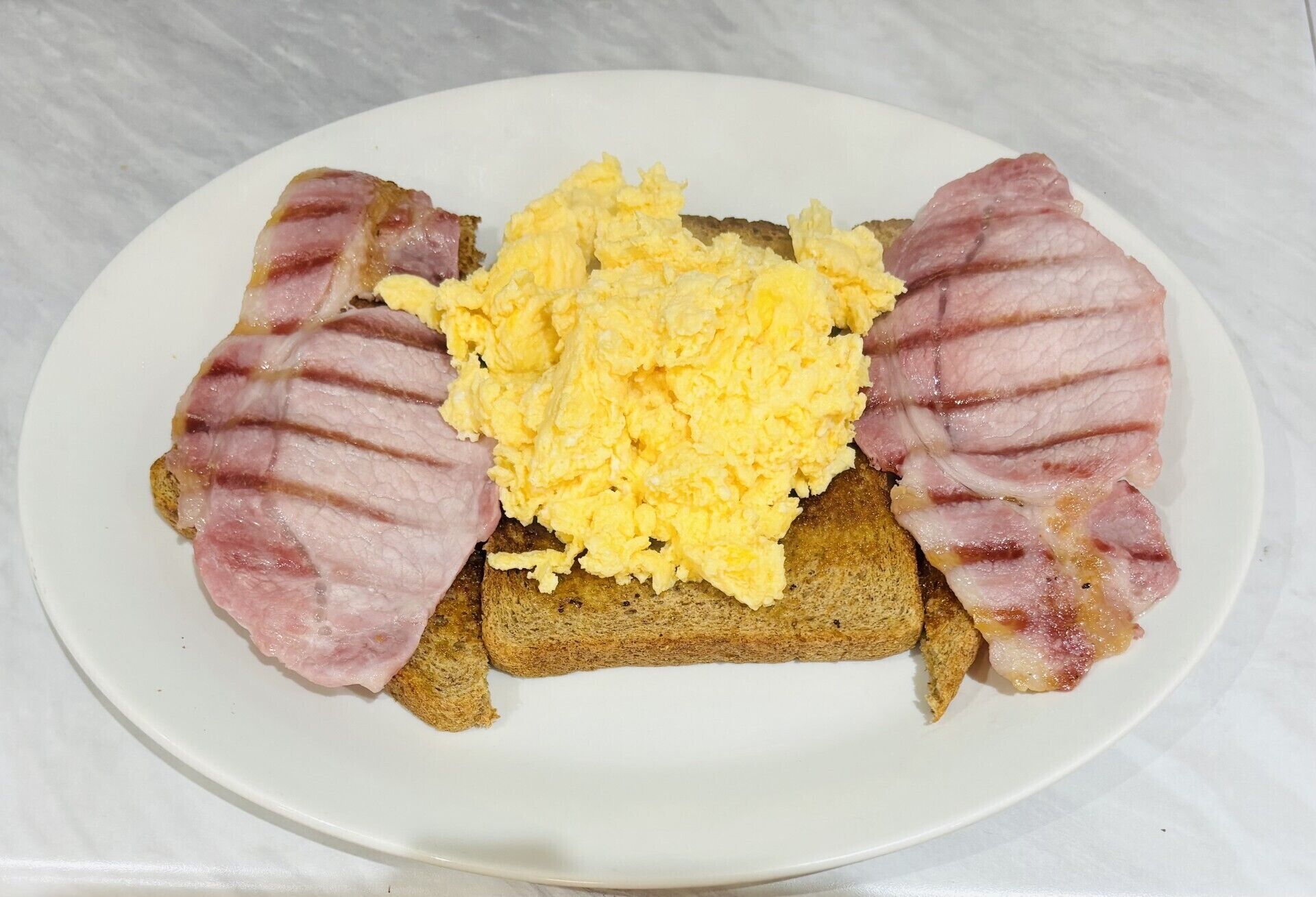 Une assiette avec des œufs brouillés, du bacon et des toasts.