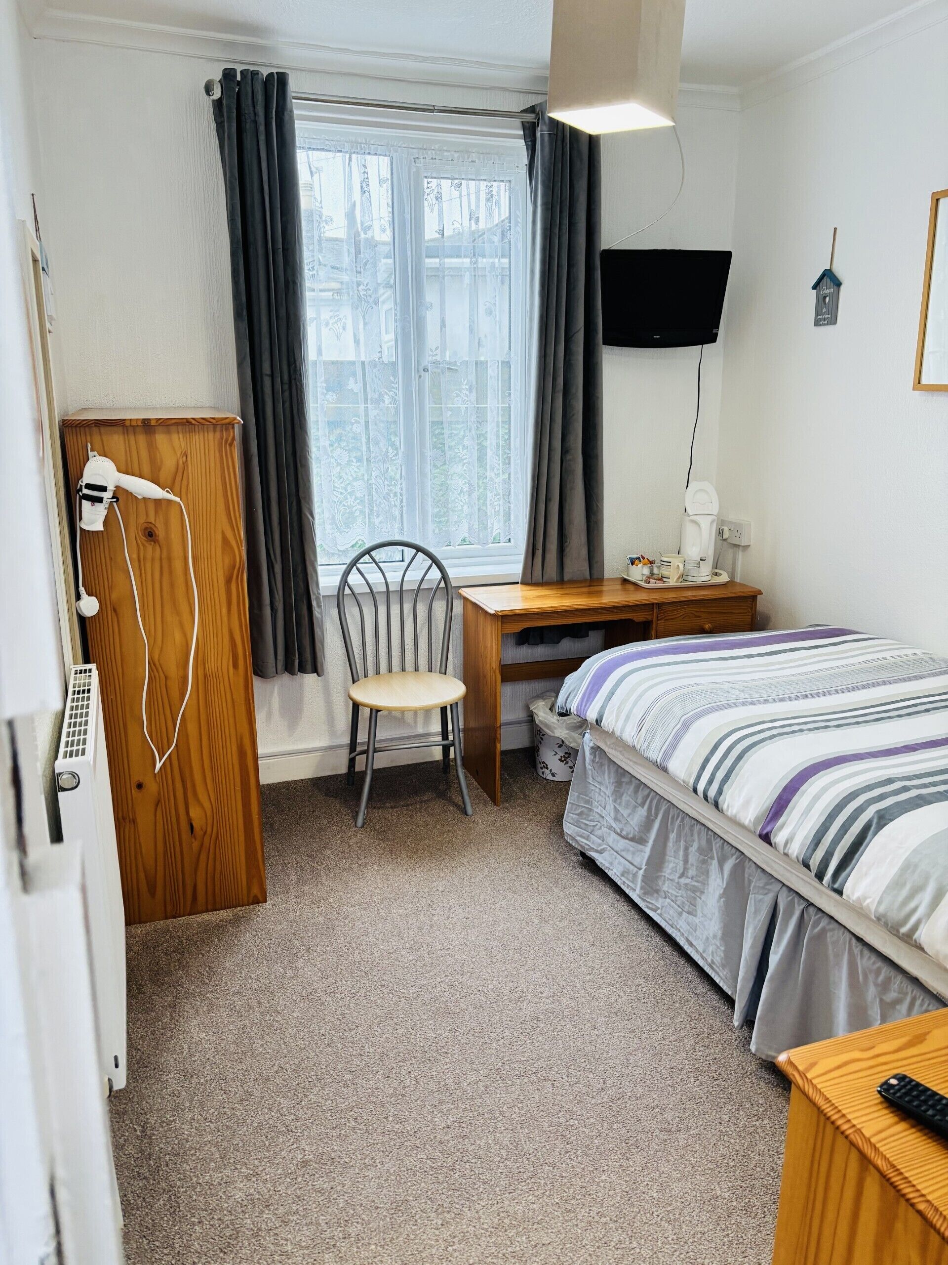 Un dormitorio con cama, escritorio, silla, televisor y ventana con cortinas.