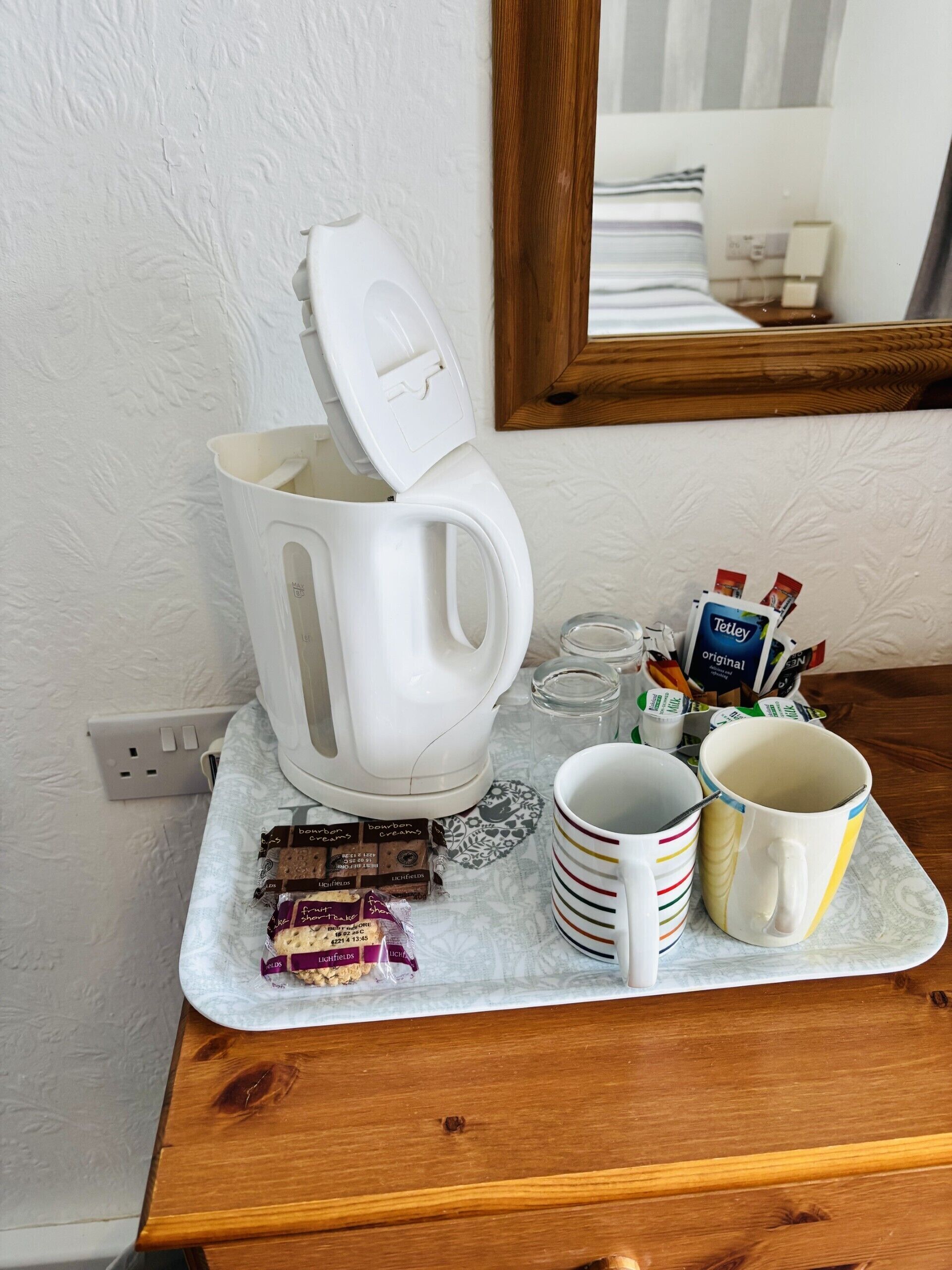 Una kitchenette con cafetera, tazas y aperitivos en una bandeja.