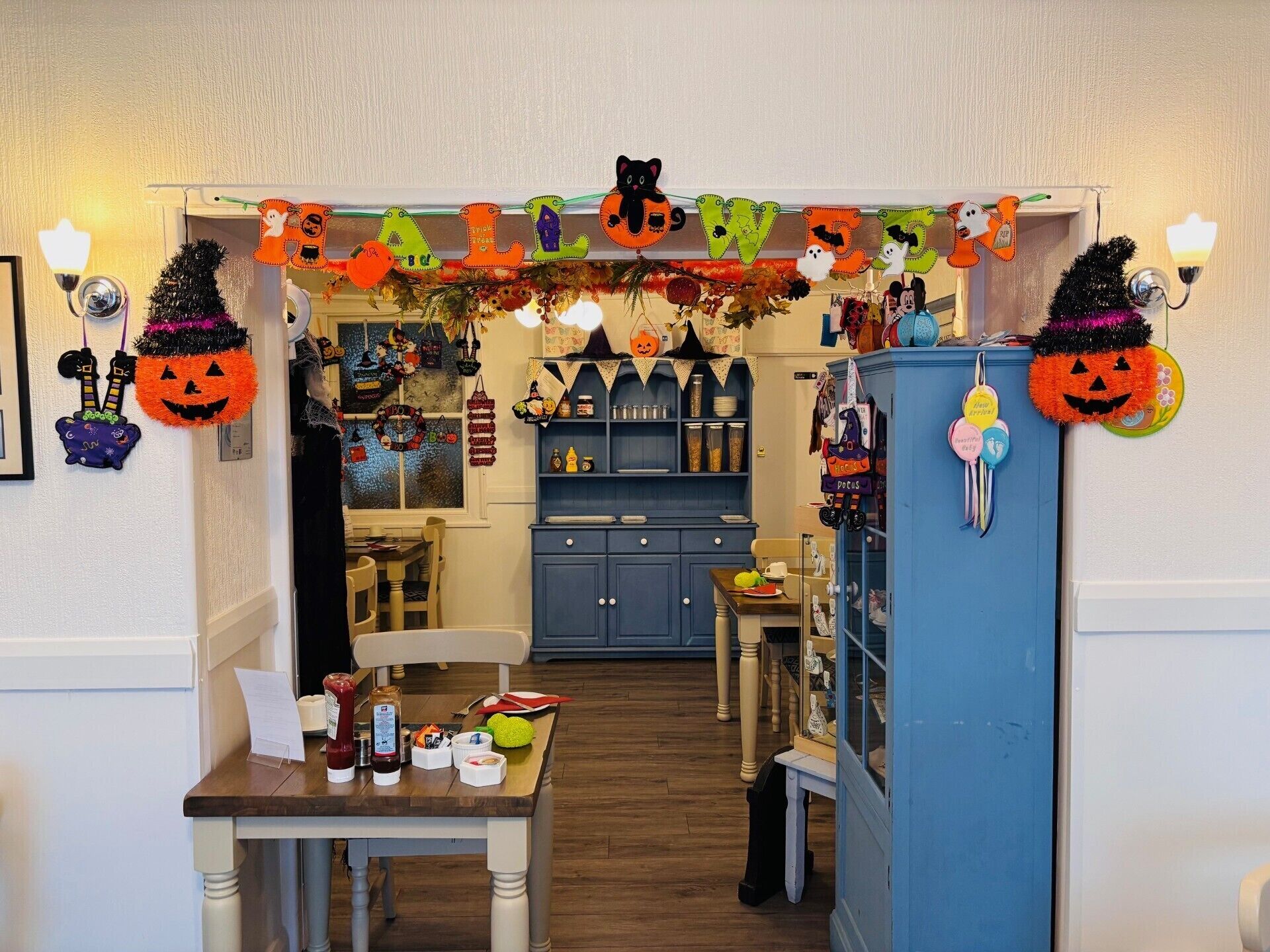 A kitchen with a festive Halloween decoration, a dining table with food items, and a blue cabinet.