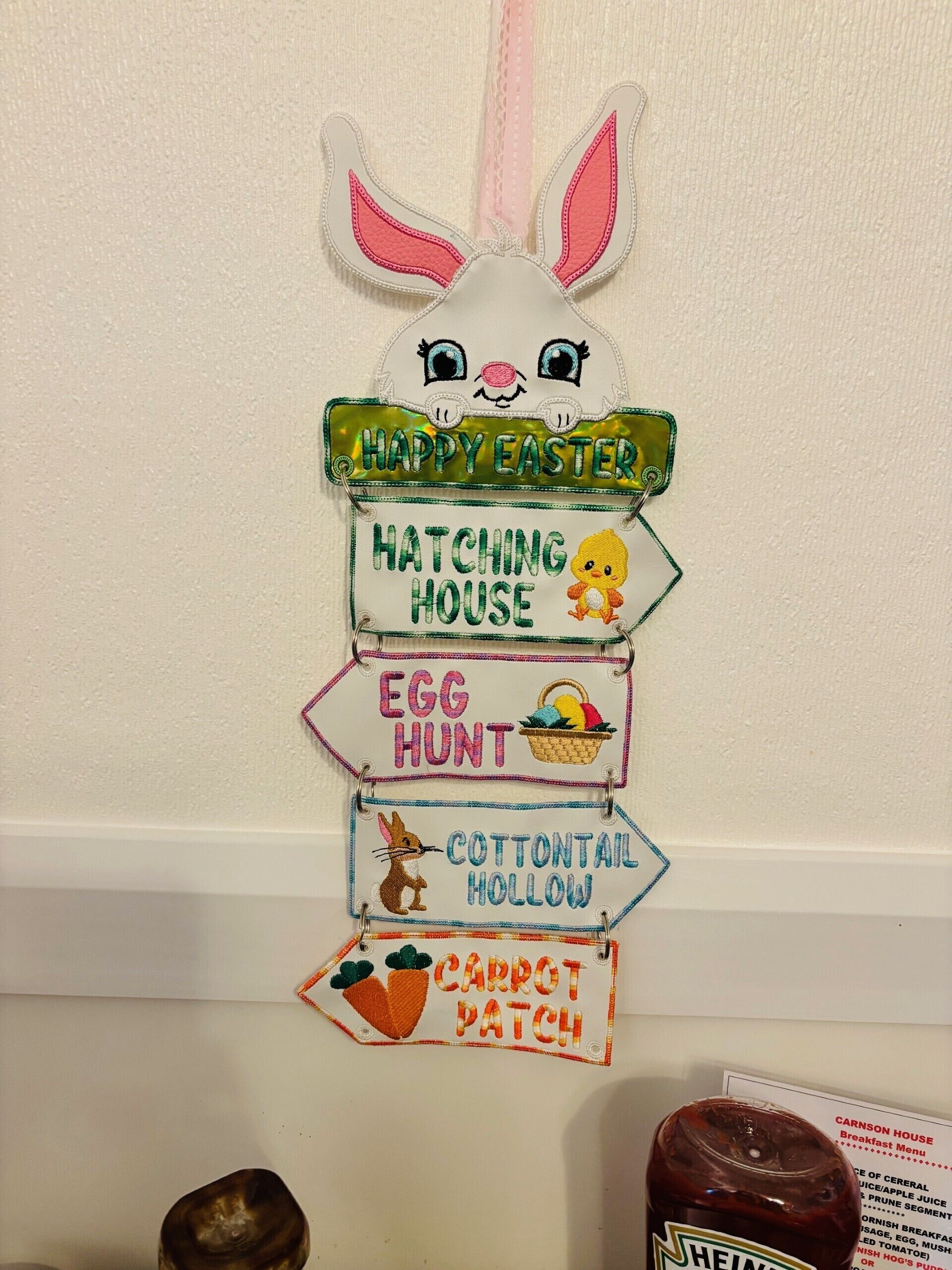 A wall decoration with a bunny head and signs for Easter activities like 'Happy Easter', 'Hatching House', 'Egg Hunt', 'Cotton Tail Hollow', and 'Carrot Patch'.