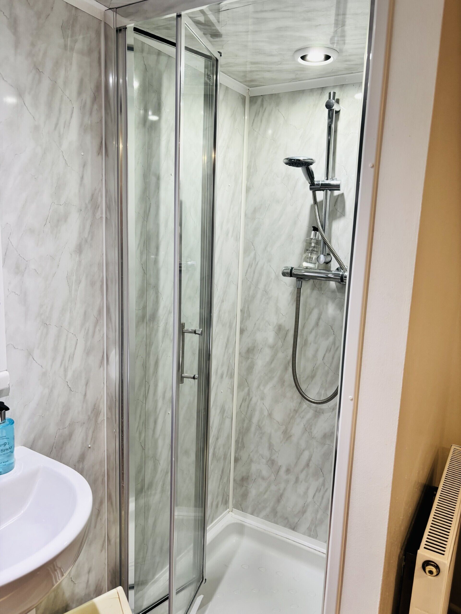 A bathroom with a glass-enclosed shower, a white sink, and a marble wall.