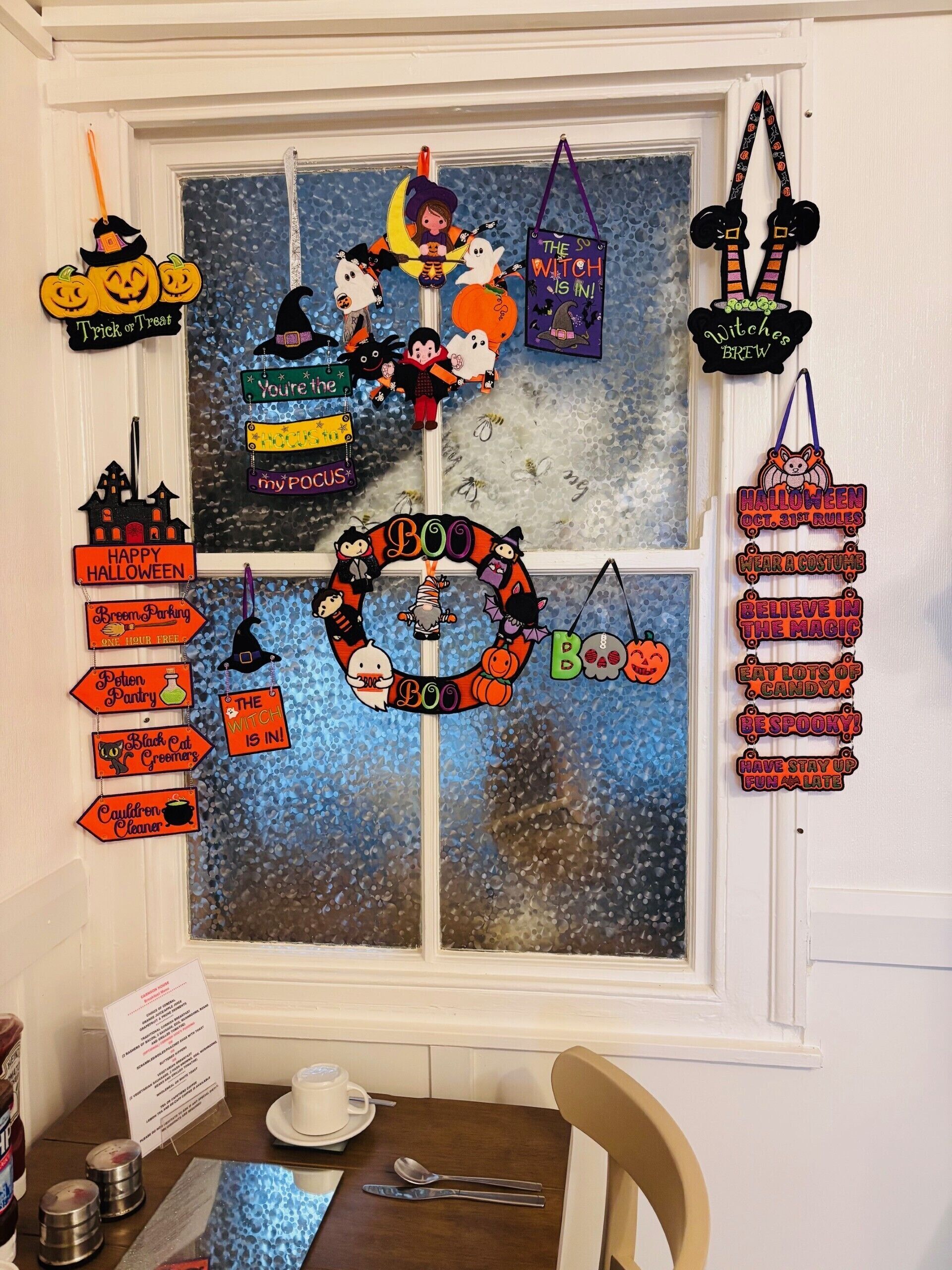 Une fenêtre décorée d’ornements sur le thème d’Halloween, notamment une pancarte sur laquelle on peut lire « Bouh ! » et divers personnages.