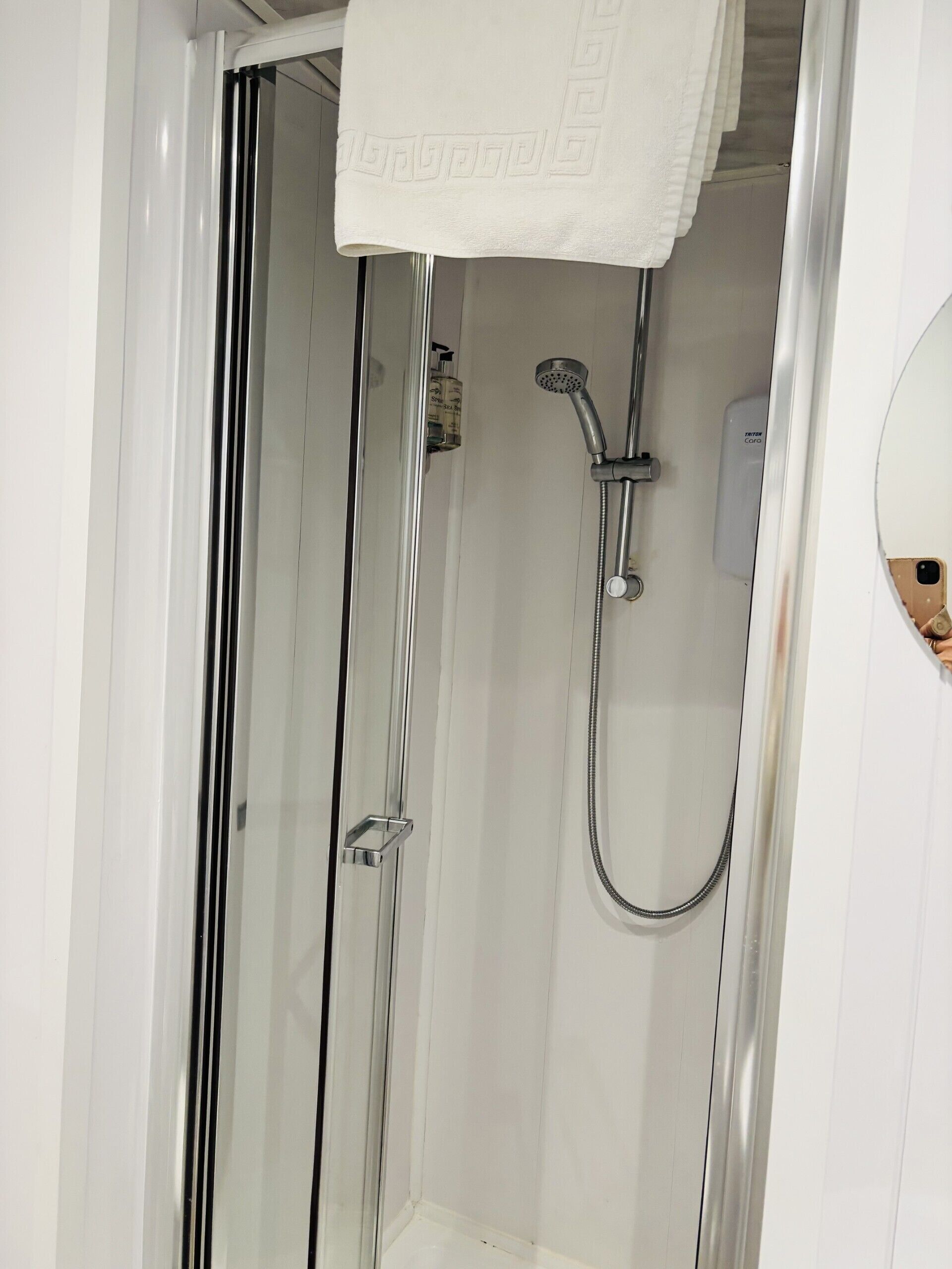 A glass-enclosed shower with a handheld showerhead and a wall-mounted faucet.