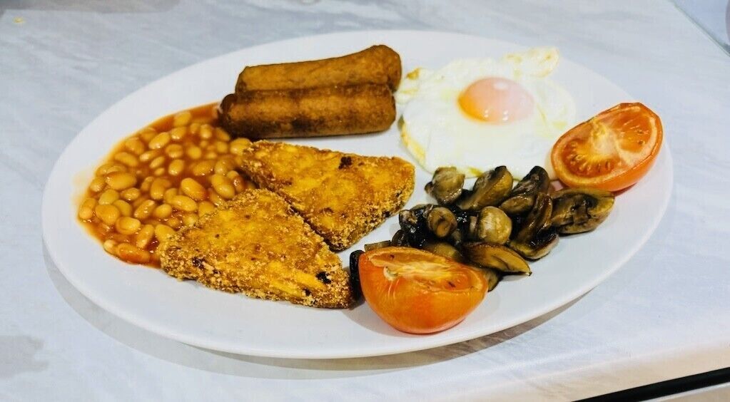 A plate of food including beans, fried fish, a fried egg, mushrooms, and a tomato.