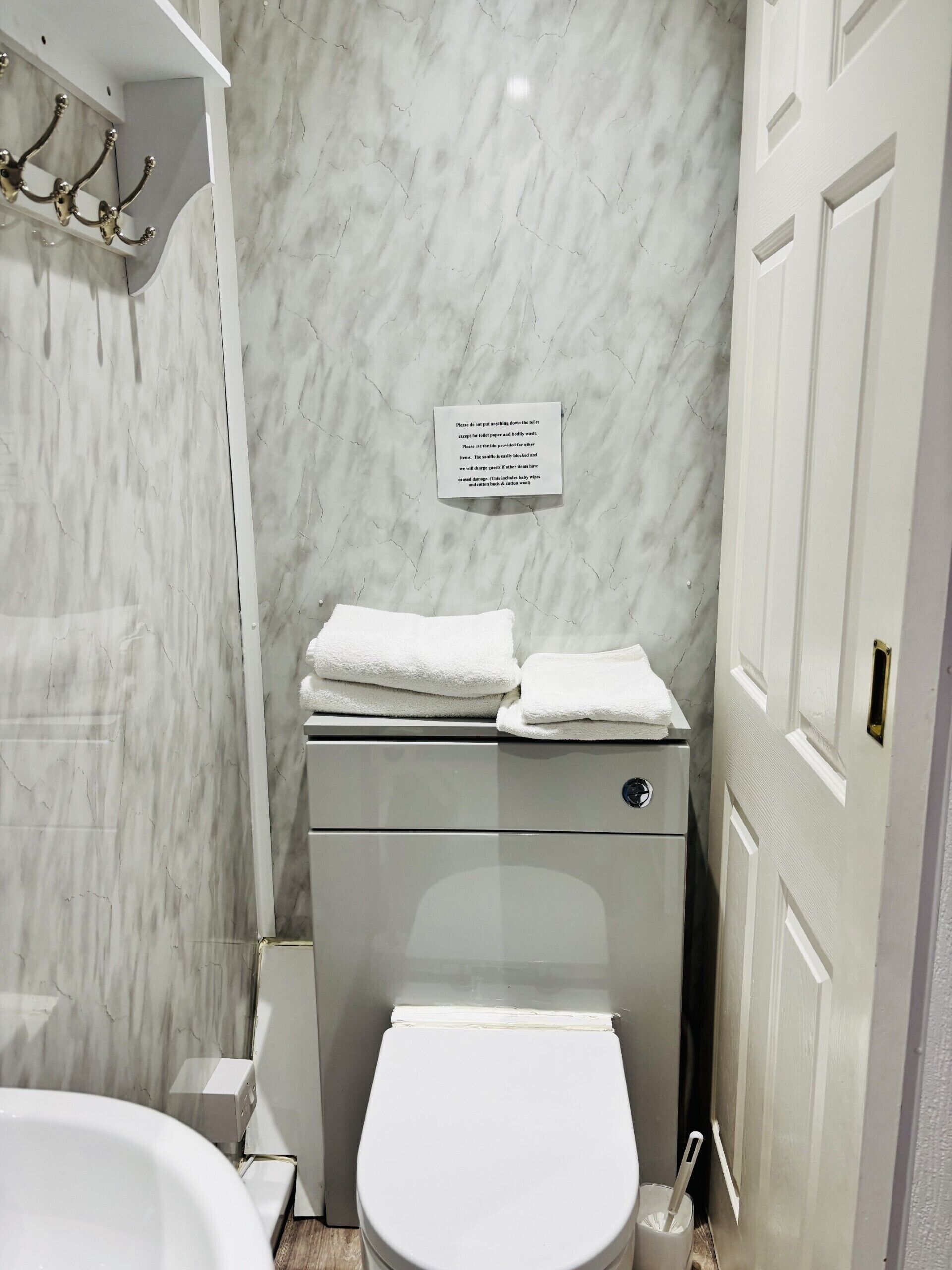 A bathroom with a toilet, a sink, and a shower area. There is a sign on the wall with instructions.