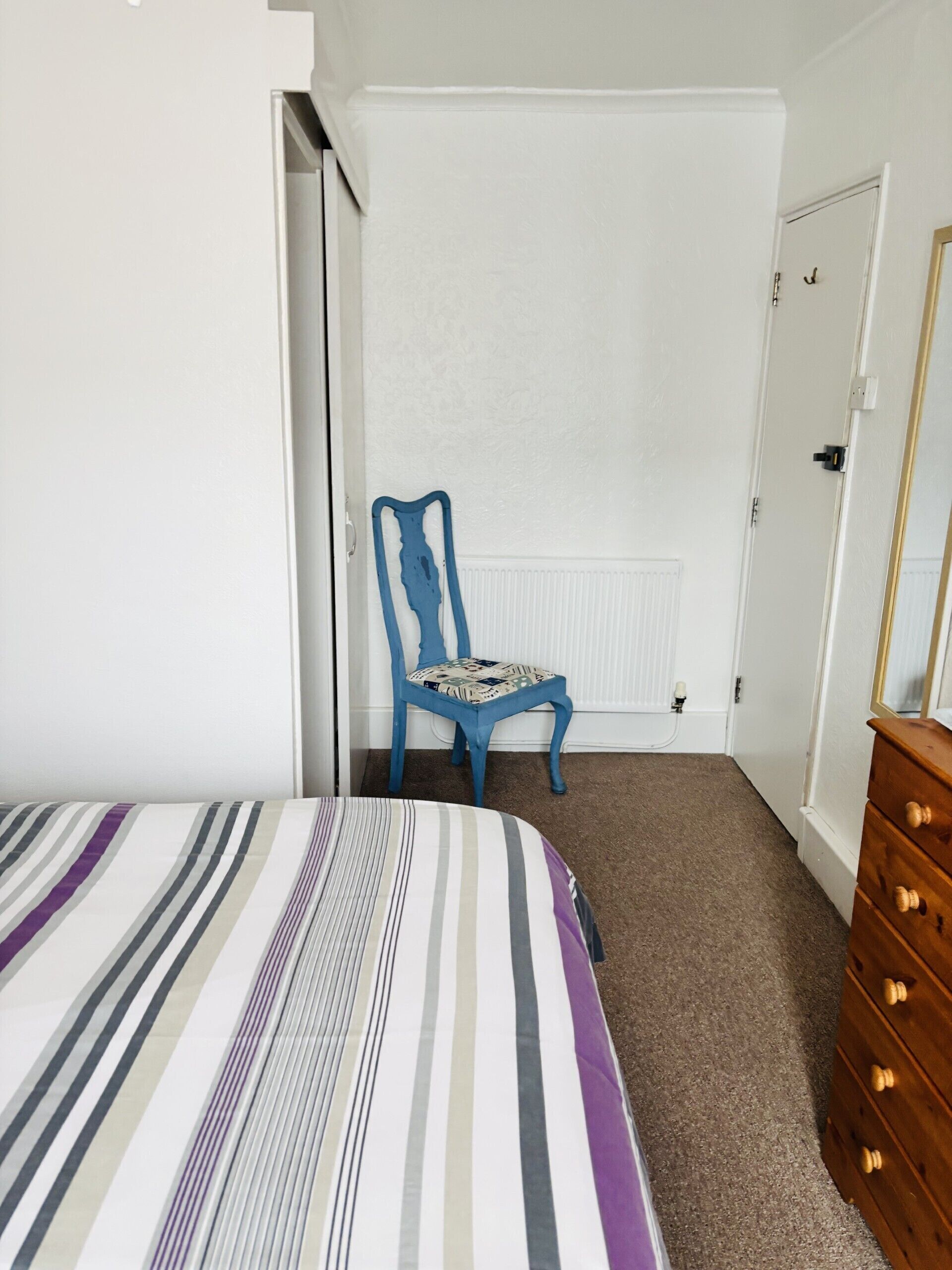 A bedroom with a bed, a blue chair, a wooden dresser, and a white door.