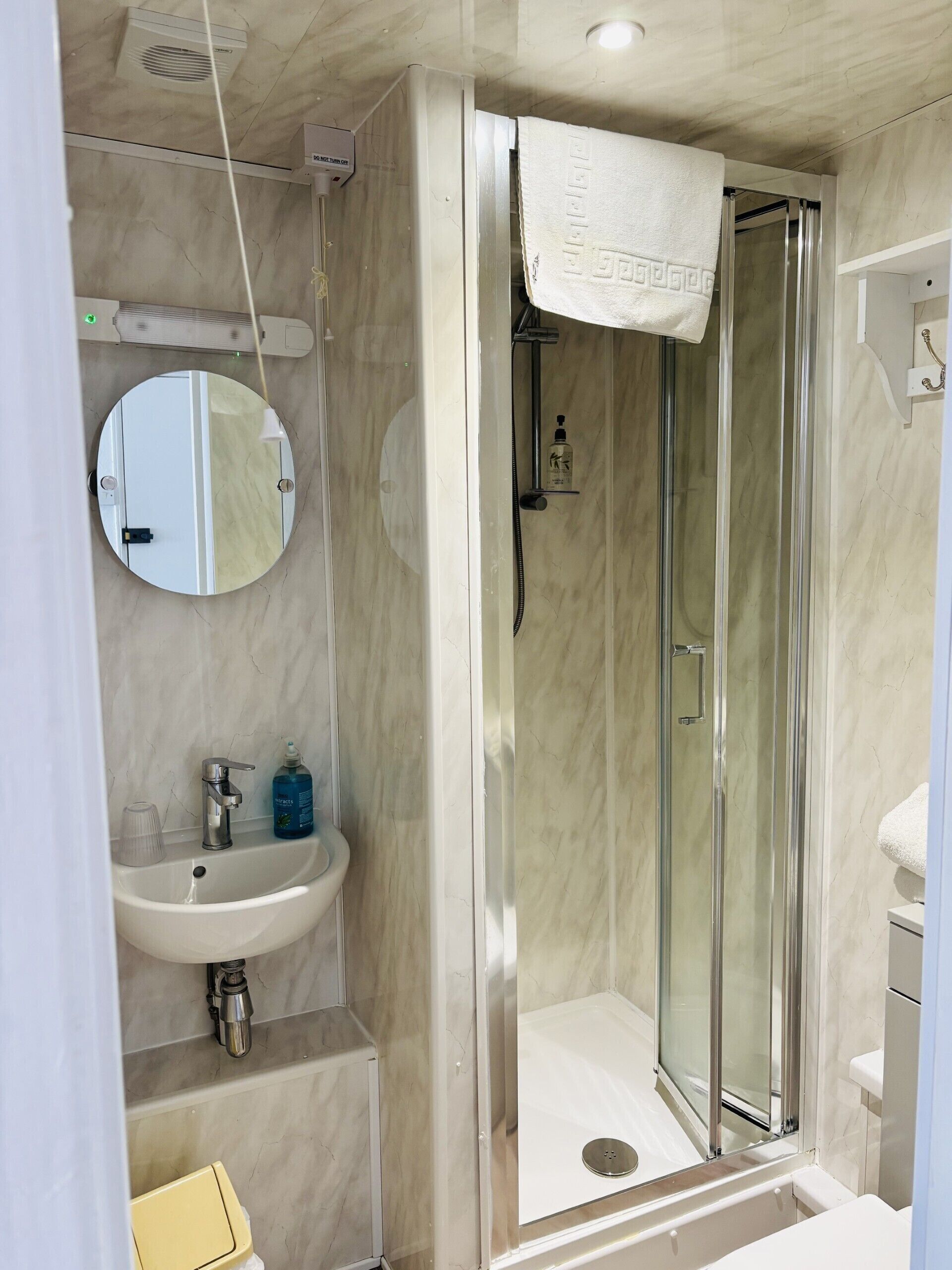 Une salle de bain moderne avec une douche à parois de verre, un miroir rond et un lavabo blanc.