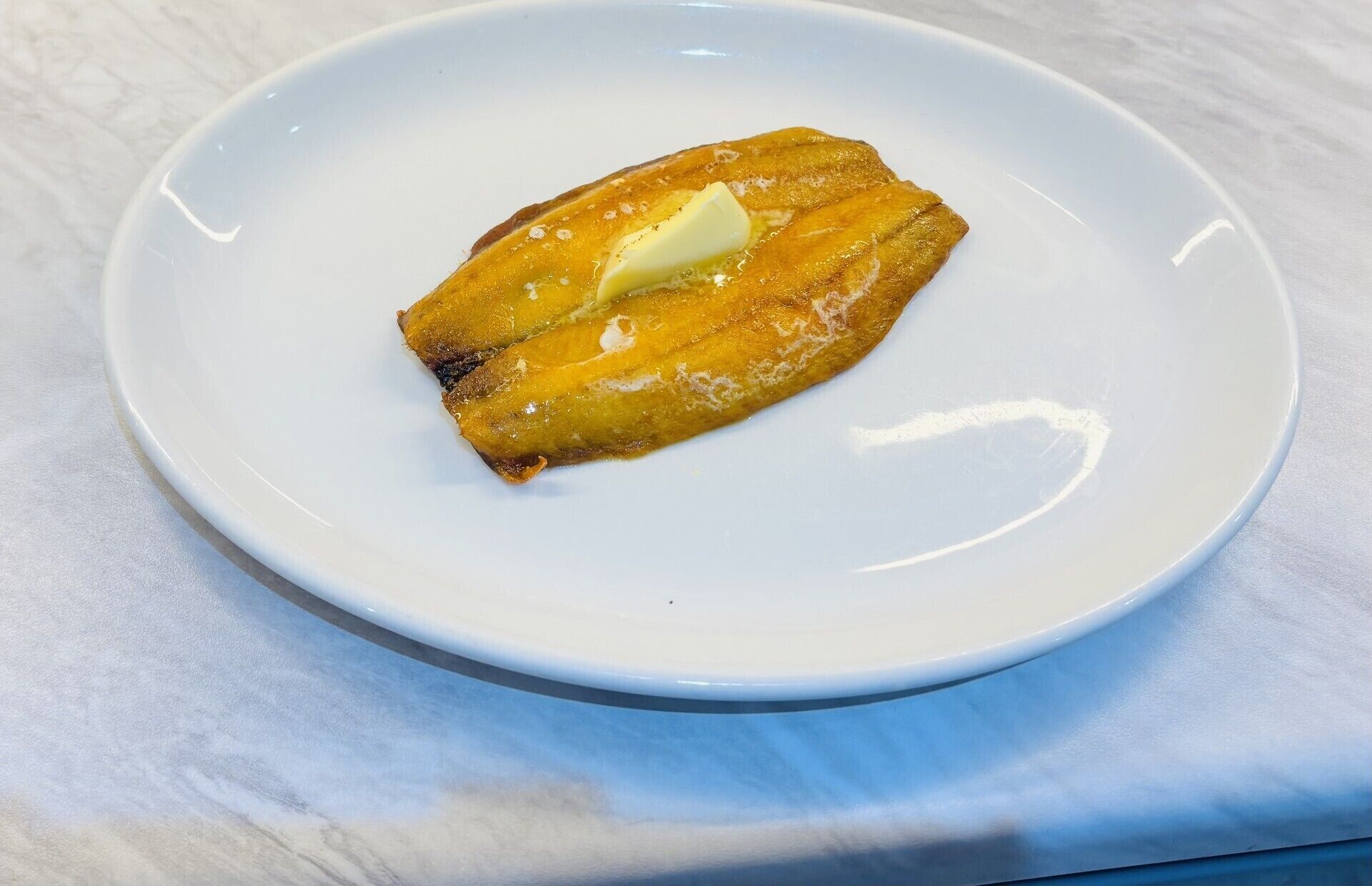 Un plato blanco con un solo bocado de comida, posiblemente un pastelito, sobre una superficie de mármol.
