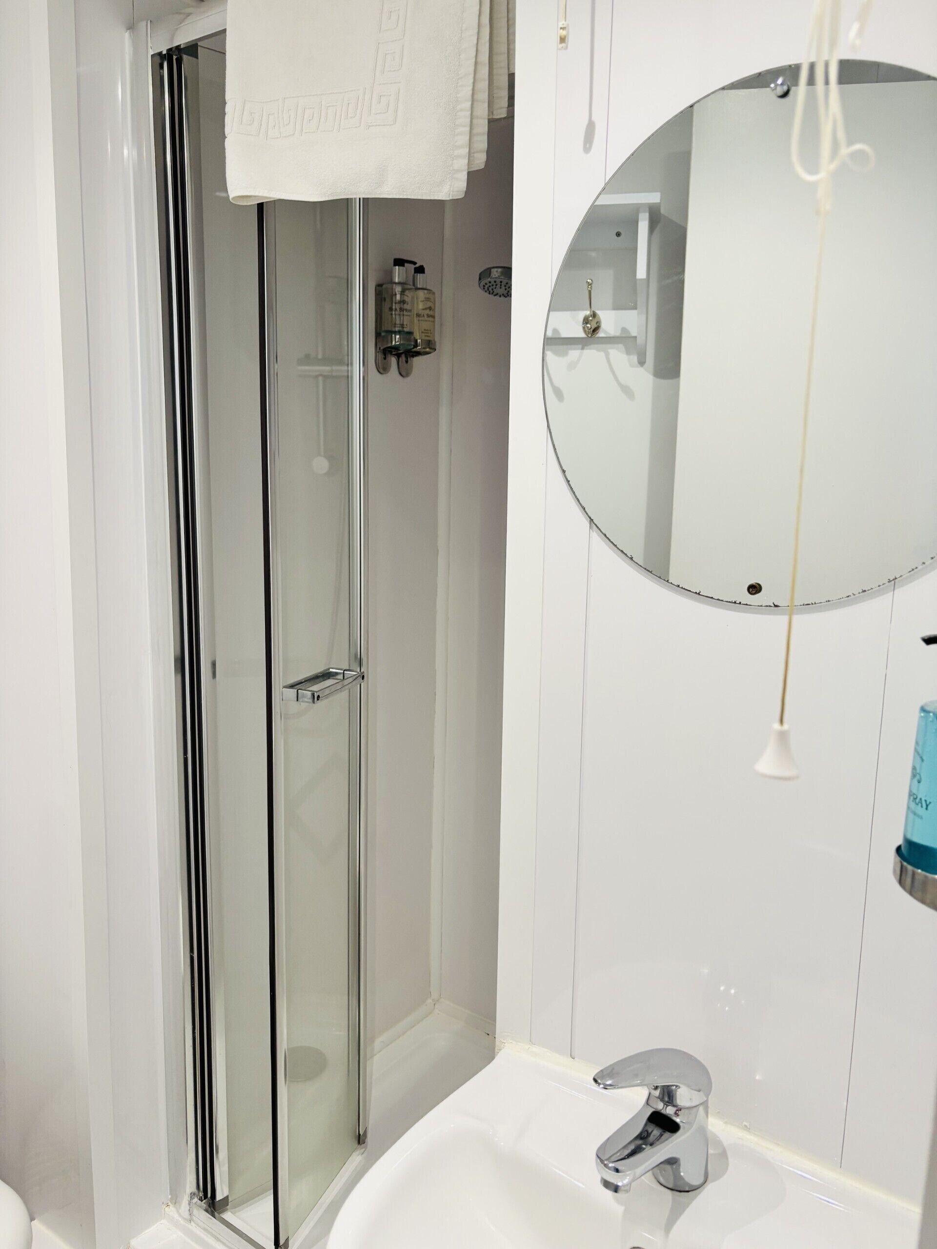 Un baño moderno con cabina de ducha de vidrio, un lavamanos blanco con grifo cromado y un espejo redondo.