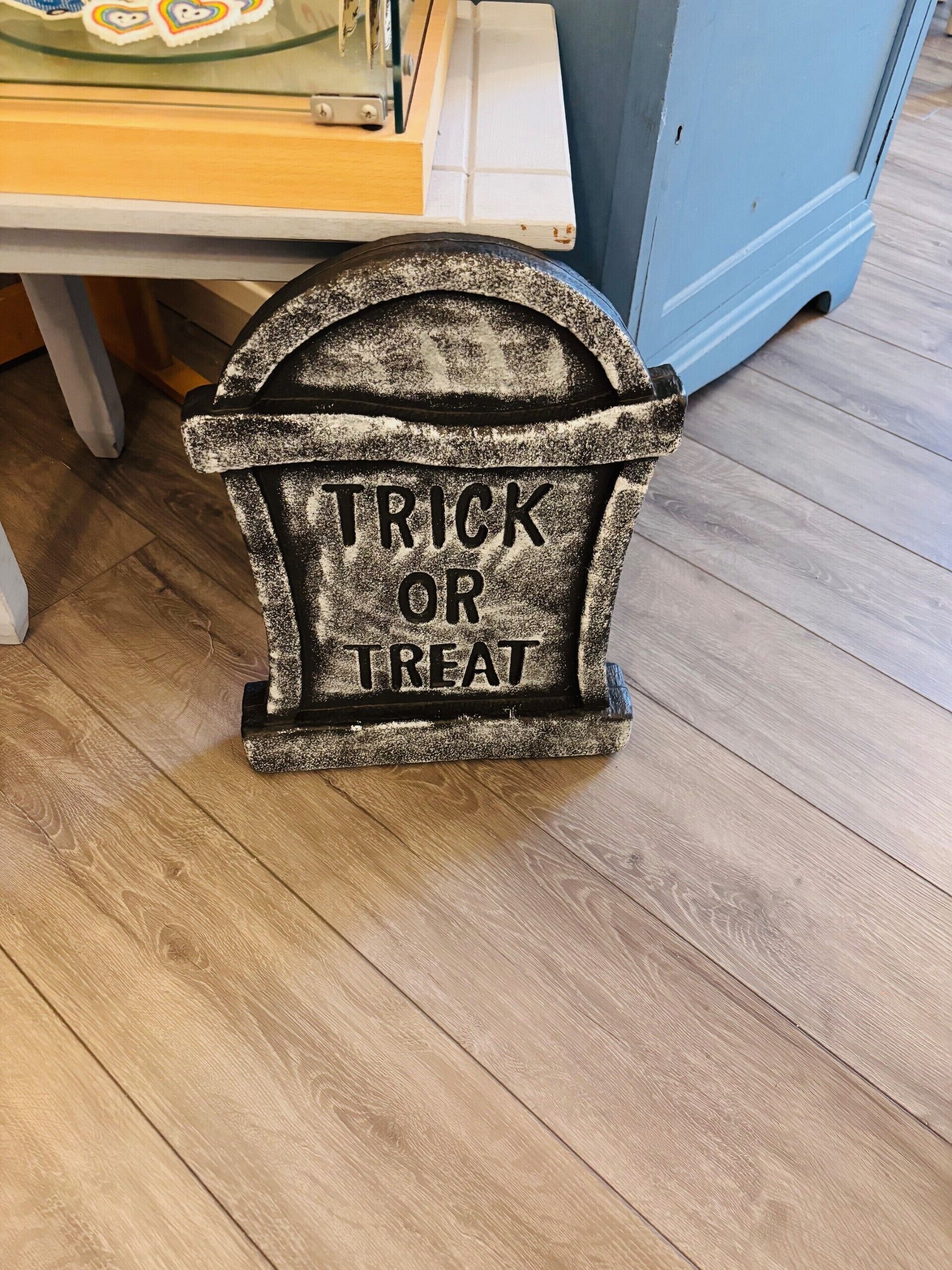 Un petit récipient de couleur sombre et à la texture particulière, portant l’inscription « TRICK OR TREAT », posé sur un plancher en bois.
