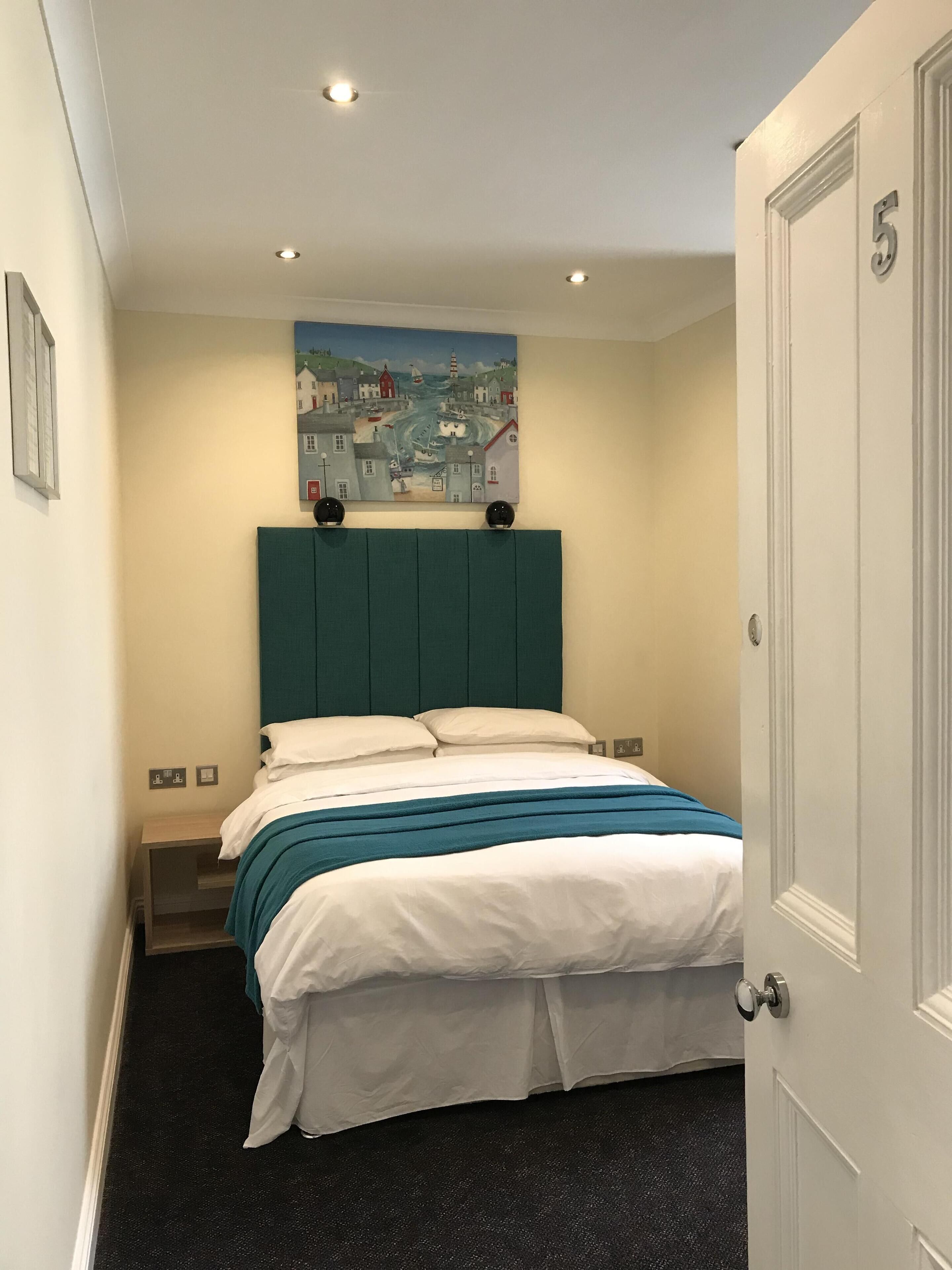 A bedroom with a bed, a headboard, a painting, and a door.