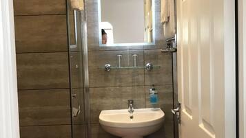 Un baño con mampara de vidrio, lavamanos pedestal y un inodoro.