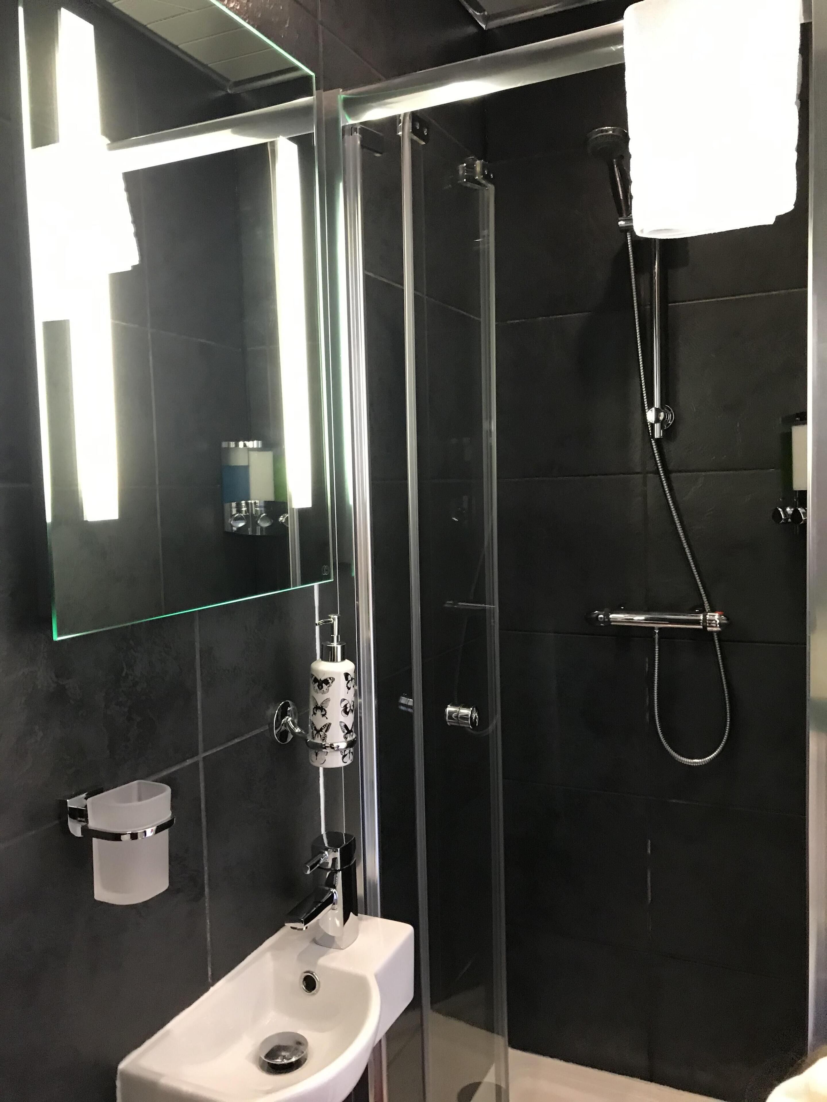Een moderne badkamer met een glazen douchecabine, een wit wastafelmeubel en een spiegel met verlichting.