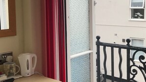 A room with a red curtain, a white kettle, and a small table with a mug and a remote control. - Cassandra Guest House (Plymouth)