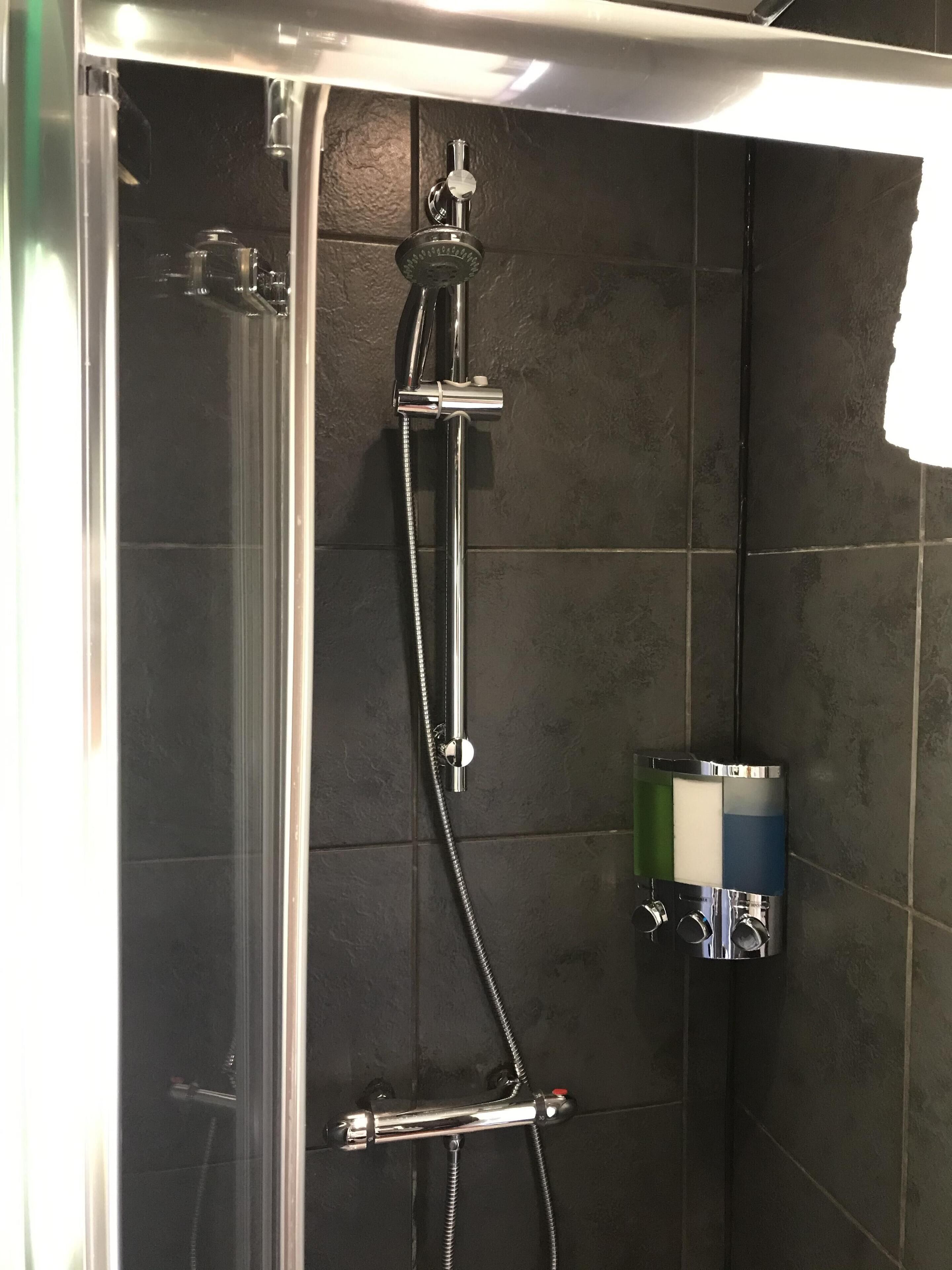 A shower with a handheld showerhead and a wall-mounted faucet, a glass door, and a towel rack.