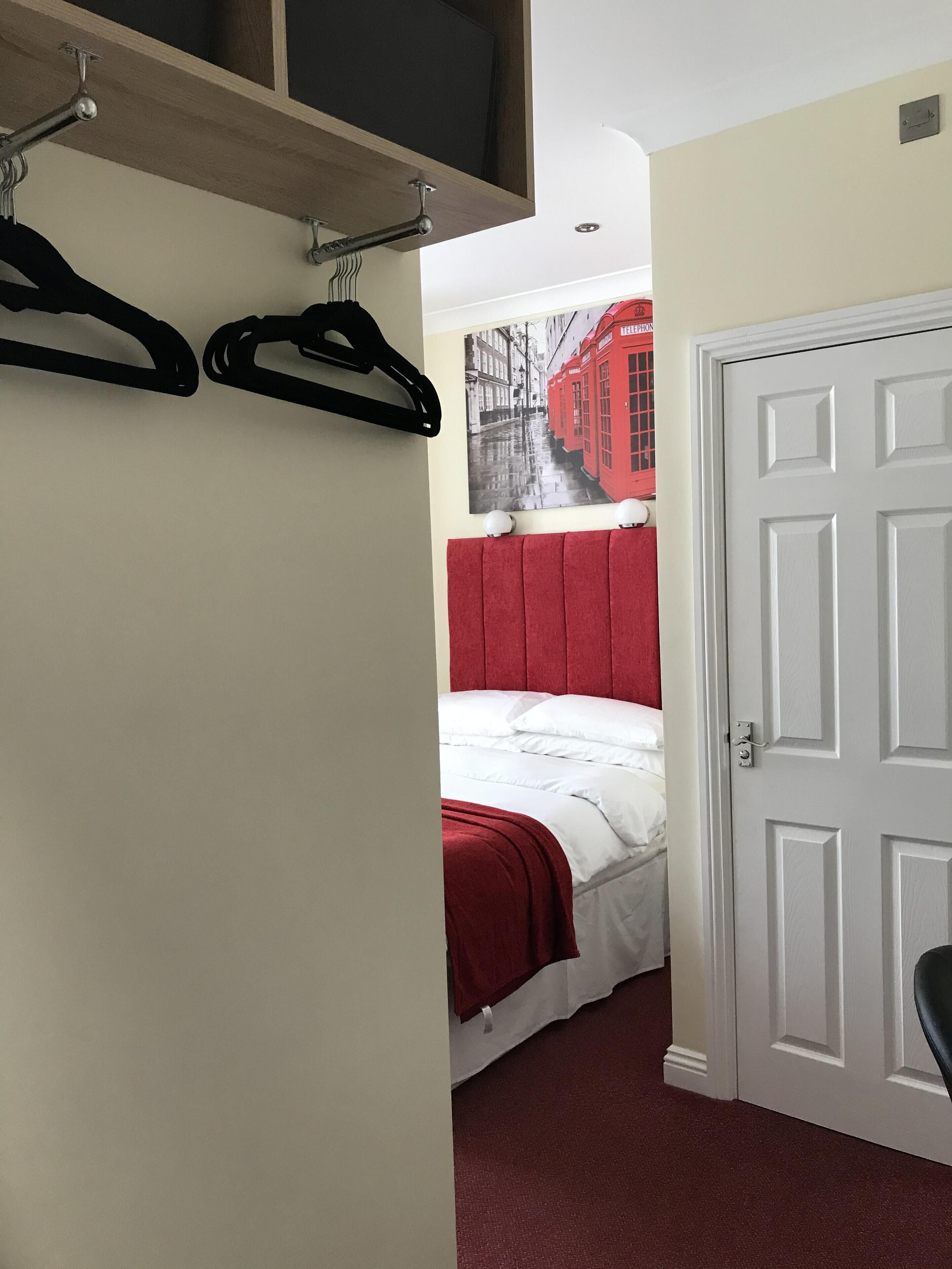 A bedroom with a bed, a red headboard, a white door, and a wall-mounted coat rack.