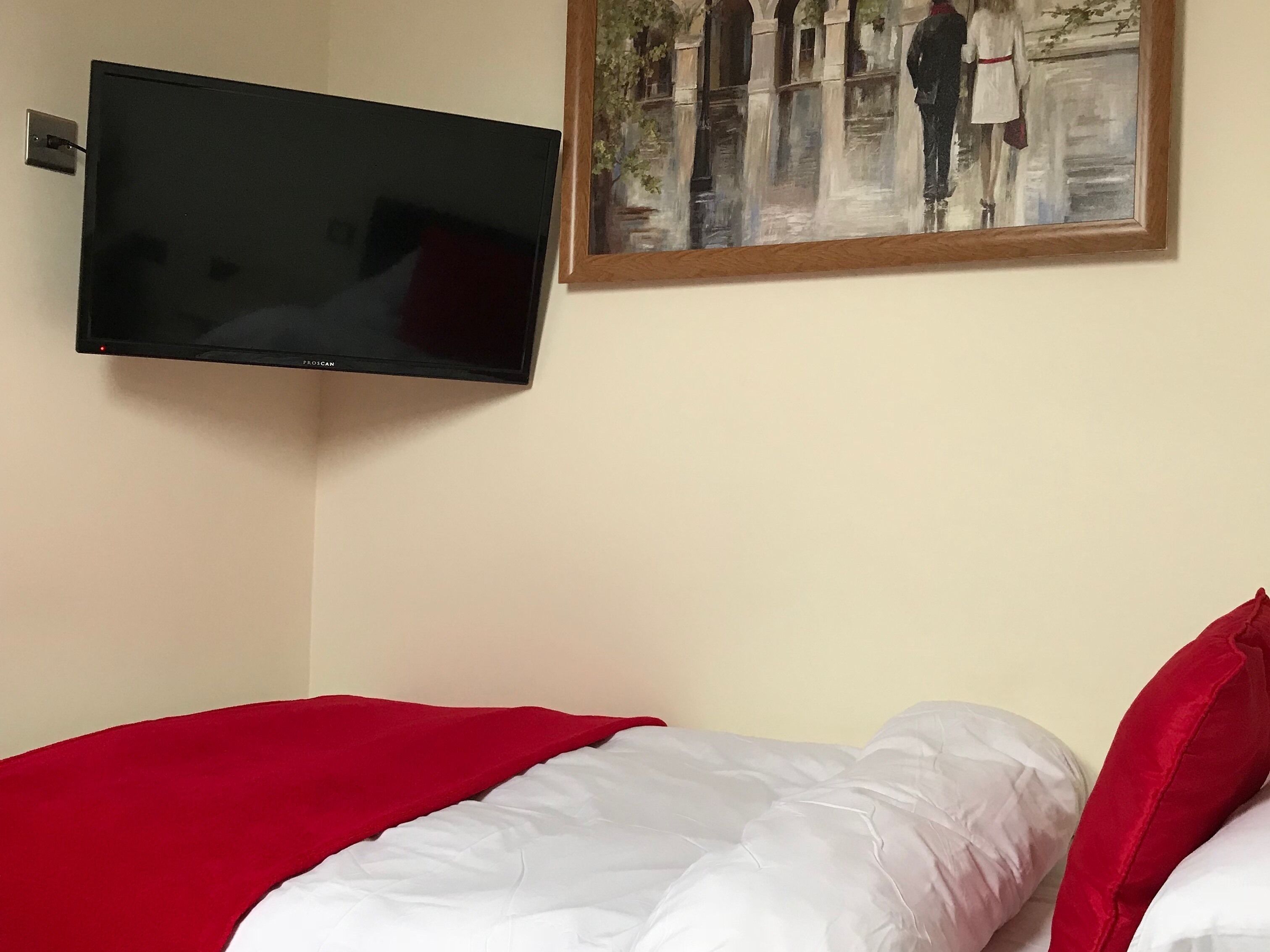 A bedroom with a bed, a television mounted on the wall, and a painting above the bed.