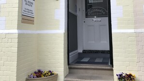 A guest house entrance with a signboard, a door with a 'NO VACANCIES' sign, and flower baskets on the steps. - Cassandra Guest House (Plymouth)