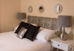 A neatly made bed with a stone headboard, two bedside tables with lamps, and three wall mirrors.