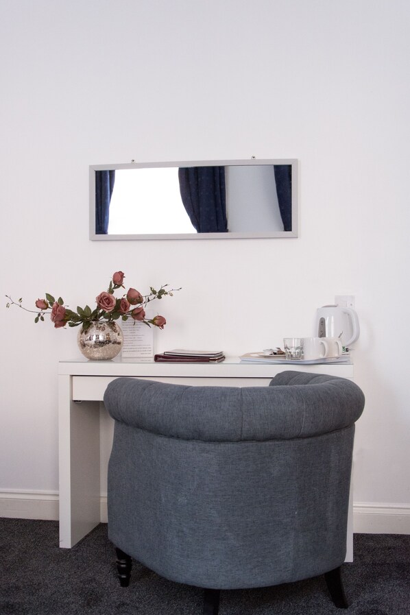 A modern room with a white desk, a grey upholstered chair, a white coffee maker, and a vase with flowers.